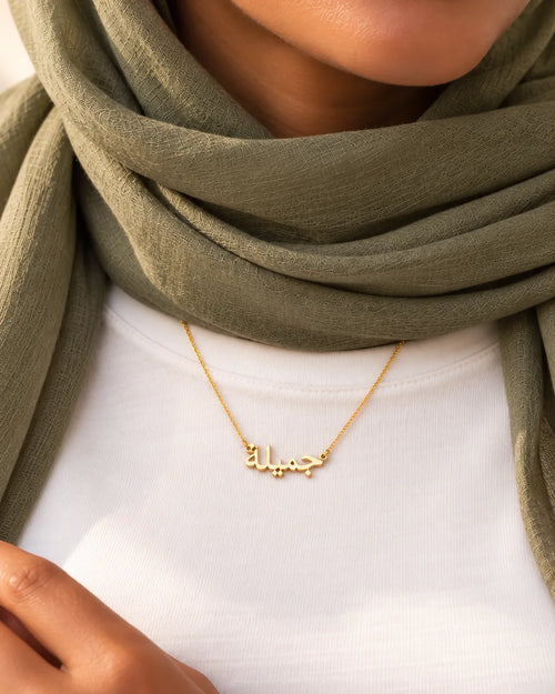 Goldene arabische Jamila-Namenskette, getragen mit olivfarbenem Kopftuch und weißem Oberteil